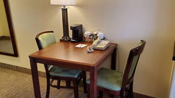 A hotel room with a wooden table, two chairs, a lamp, a coffee maker, and a telephone.