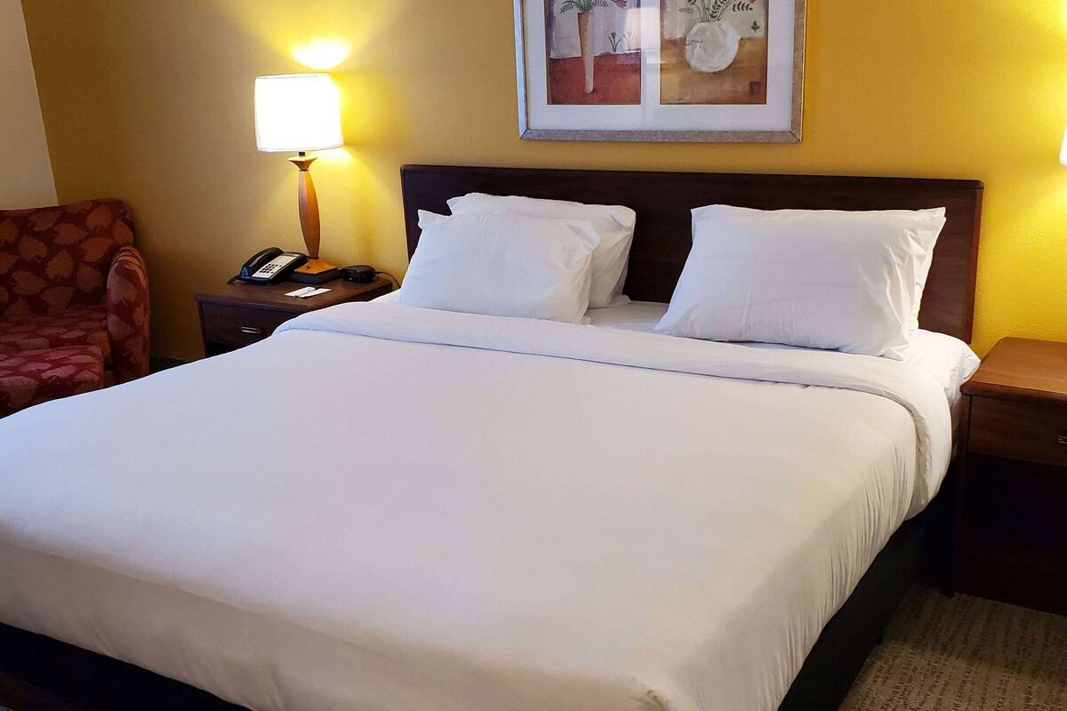 A neatly made bed with white linens, a wooden headboard, and a bedside lamp.