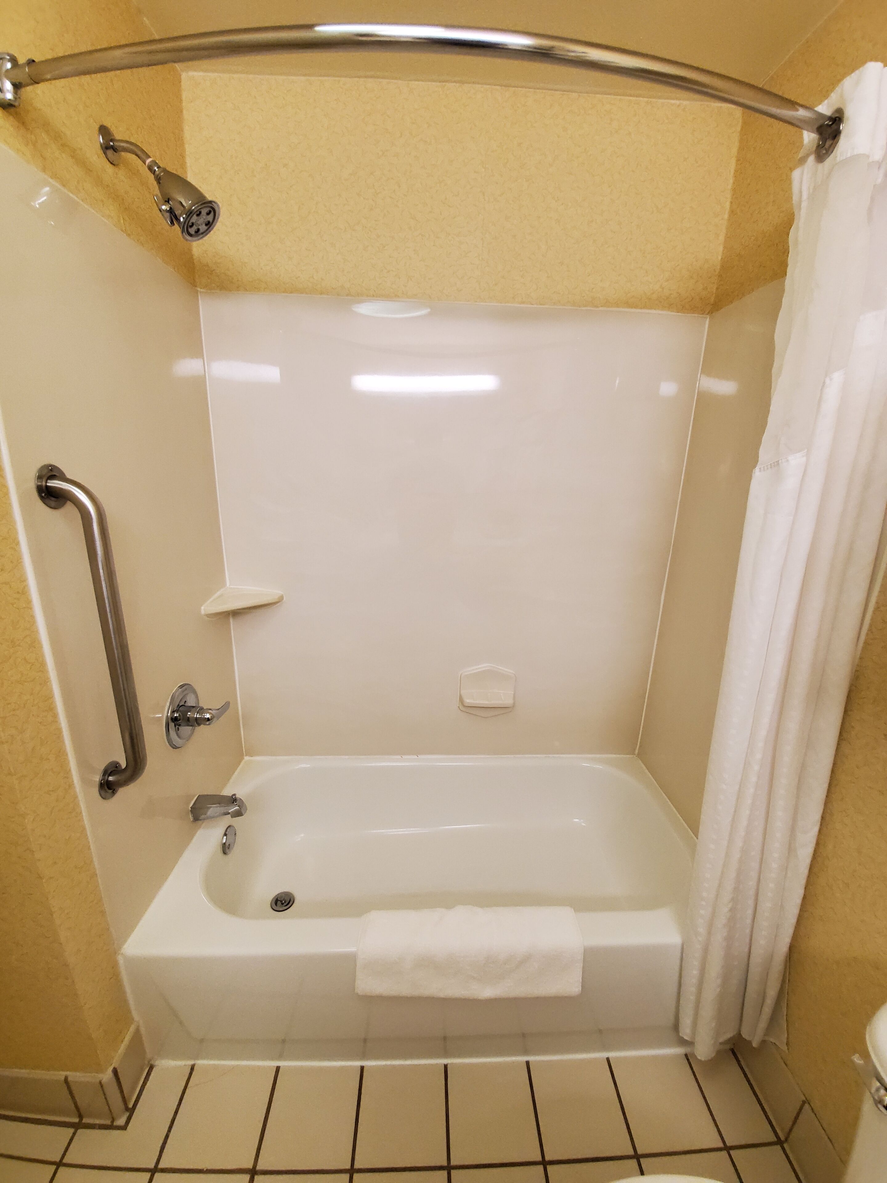 A standard bathroom with a bathtub, a shower, a handrail, and a towel rack.