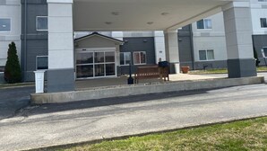 A modern building with a covered entrance, a bench, and a potted plant. - Wingate by Wyndham Uniontown (Uniontown)