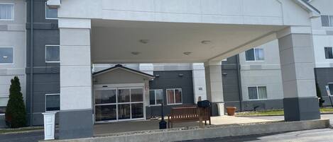 A modern building with a covered entrance, a bench, and a potted plant.