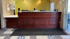 A reception area with a wooden counter, a yellow wall, and a black mat with social distancing markings. - Wingate by Wyndham Uniontown (Uniontown)