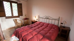A bedroom with a large bed, a chair, a nightstand, and a window with curtains. - Agriturismo Baglio Donna Santa (Paceco)