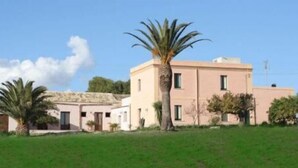 A two-story building with a flat roof and a large palm tree in the front. - Agriturismo Baglio Donna Santa (Paceco)