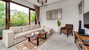 A modern living room with a beige sofa, a wooden coffee table, a wicker armchair, and a TV on a wooden stand. - Villa Daana Uluwatu (Ungasan)