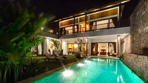 A modern two-story house with a swimming pool, outdoor seating, and a well-lit interior. - Villa Daana Uluwatu (Ungasan)