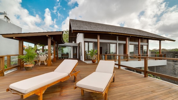 A wooden deck with two lounge chairs and a covered area with a table and chairs. - Villa Daana Uluwatu (Ungasan)