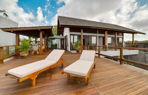 A wooden deck with two lounge chairs and a covered area with a table and chairs. - Villa Daana Uluwatu (Ungasan)