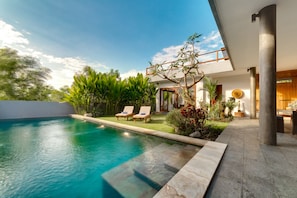 A modern house with a swimming pool, two lounge chairs, and a garden with various plants.