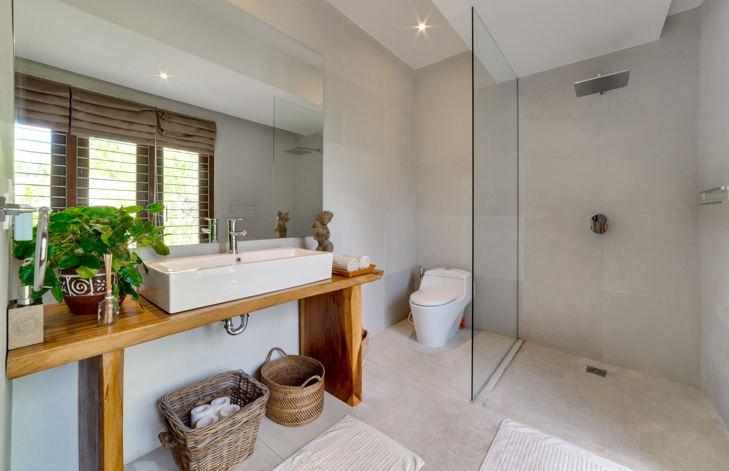 Un baño moderno con un espejo grande, tocador de madera, lavamanos blanco y mampara de ducha de vidrio.