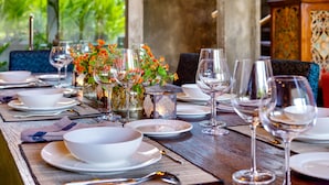 A table set for dining with white plates, bowls, and wine glasses, surrounded by chairs and a decorative centerpiece. - Villa Daana Uluwatu (Ungasan)