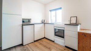 Une cuisine de taille réduite avec des meubles blancs, un four à micro-ondes, une cuisinière et une fenêtre dotée de stores bleus.