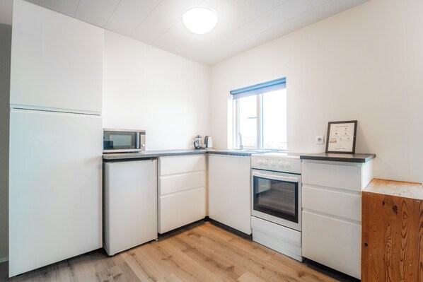 A compact kitchen with white cabinets, a microwave, a stove, and a window with blue blinds.