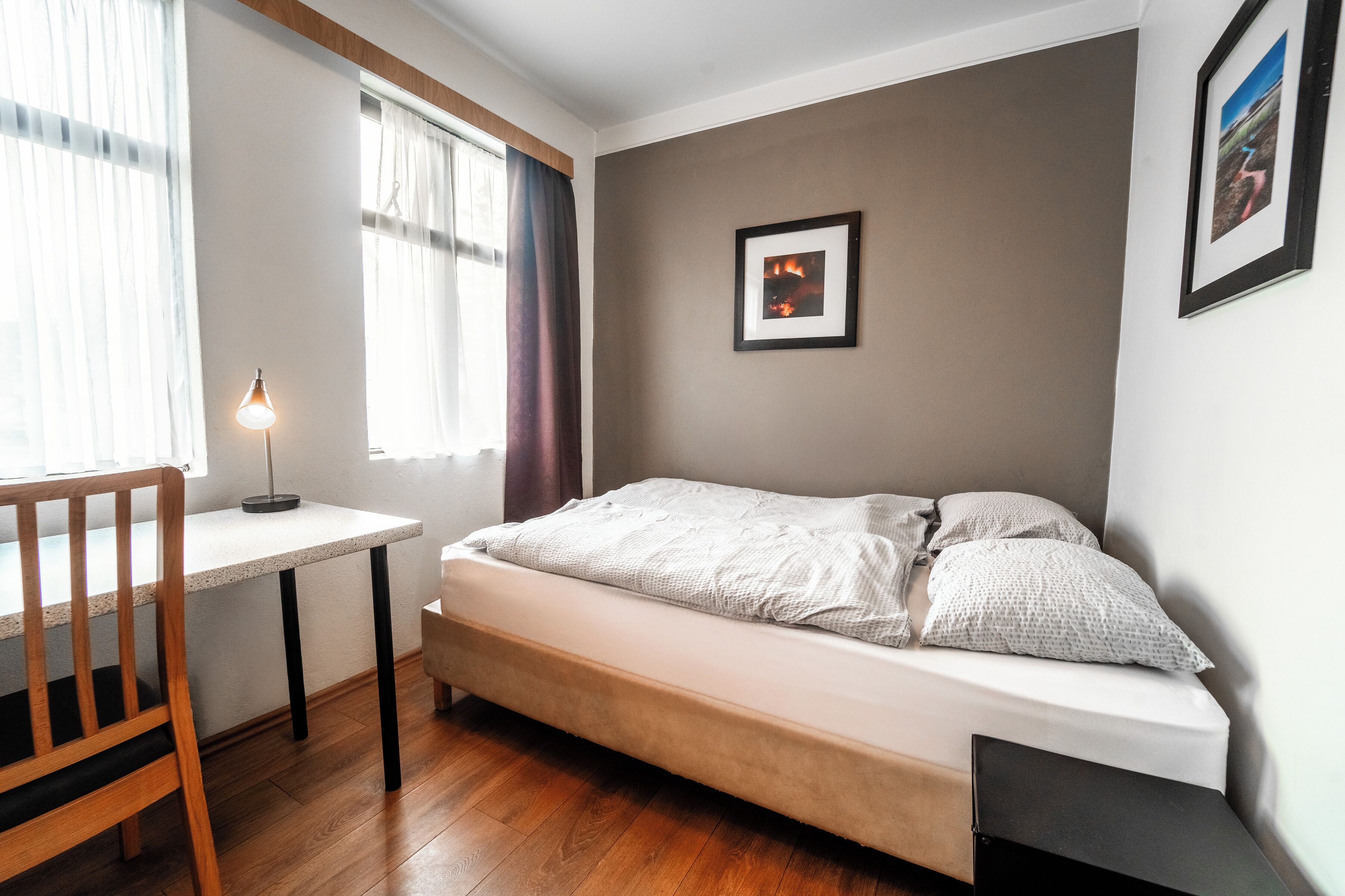 Une chambre à coucher avec un lit, un bureau, une chaise et une fenêtre avec des rideaux.