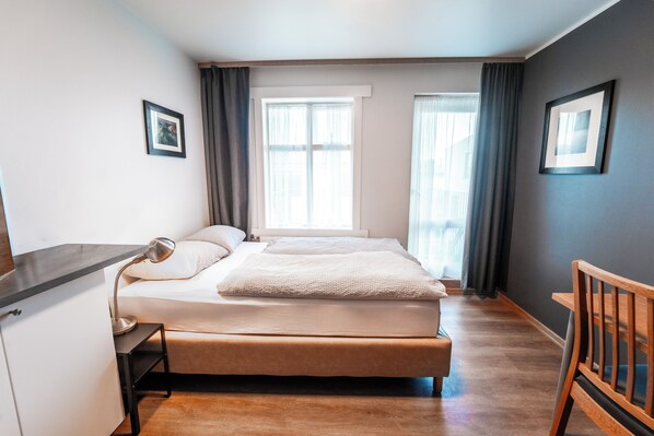 A bedroom with a bed, bedside table, wardrobe, and a wooden chair. - Guesthouse Andrea (Reykjavik)