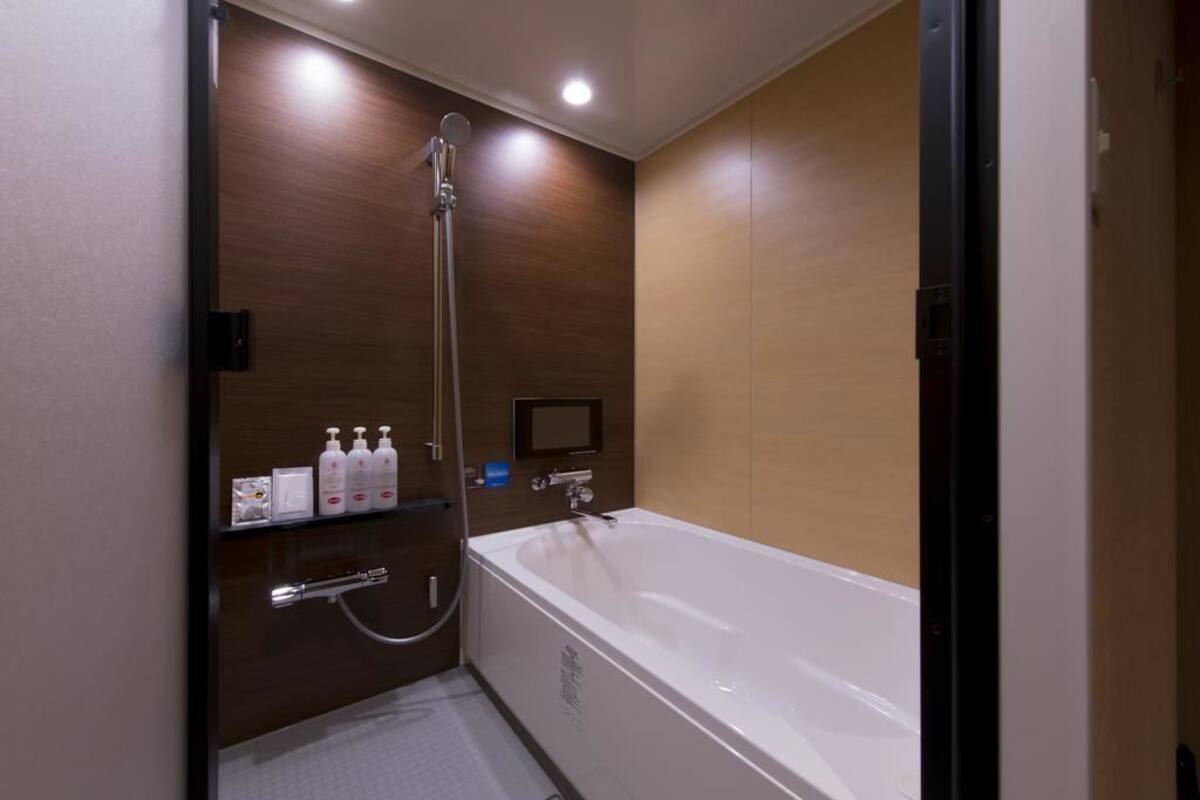 A modern bathroom with a large bathtub, a showerhead, and a shelf with toiletries.