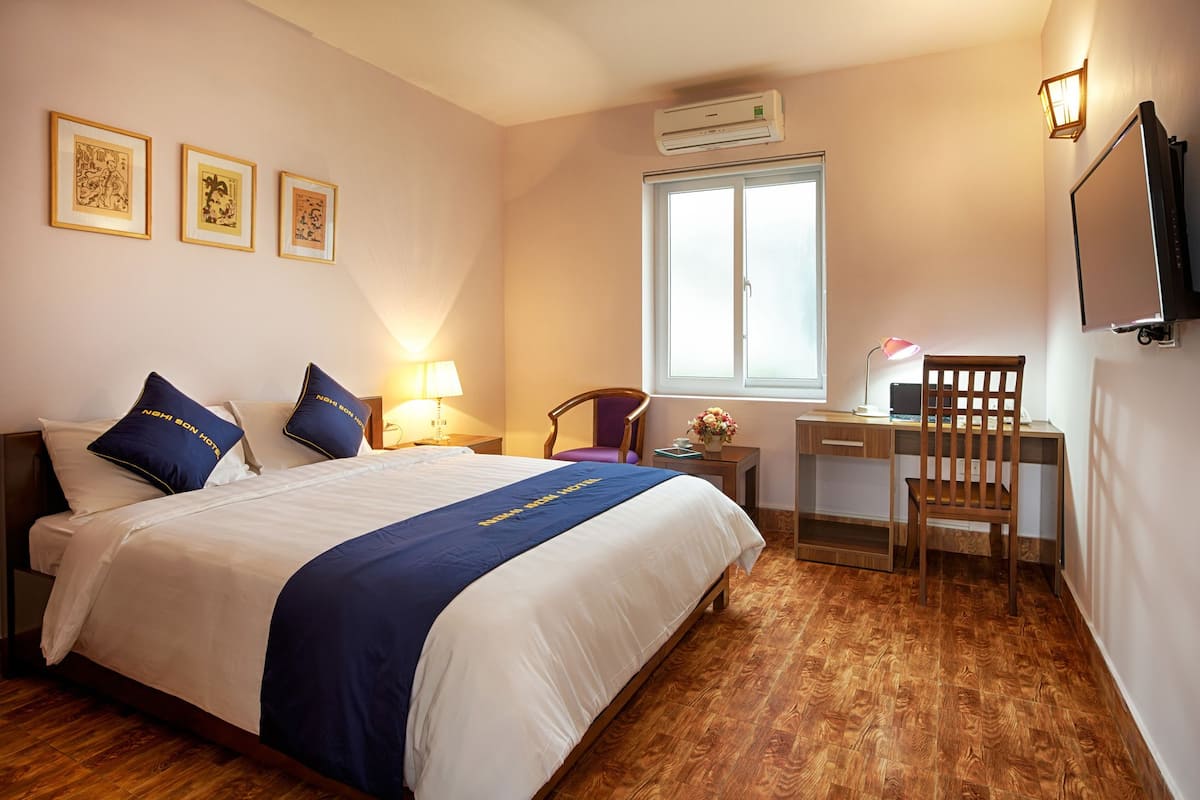 Ett hotellrum med en säng, ett skrivbord, en stol, en tv och konstverk på väggen.