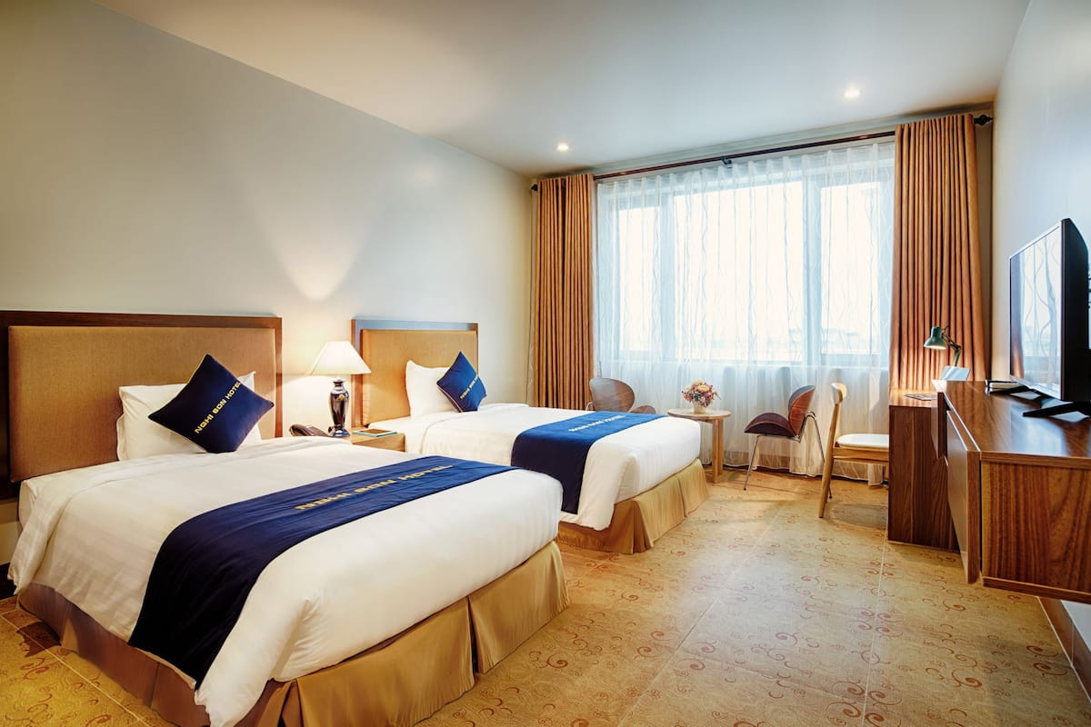 Ett hotellrum med två sängar, ett skrivbord, en stol, en TV och ett fönster med gardiner.
