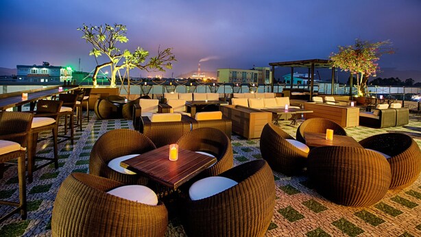 Een terras met rieten meubels en uitzicht op de skyline bij zonsondergang.