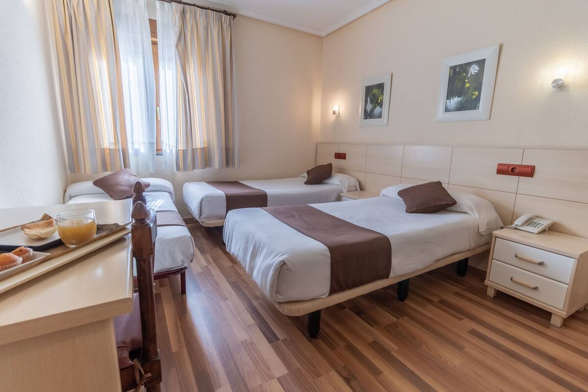 Quarto de hotel com duas camas de solteiro, piso de madeira, escrivaninha pequena com bandeja de comida e mesa de cabeceira com telefone.