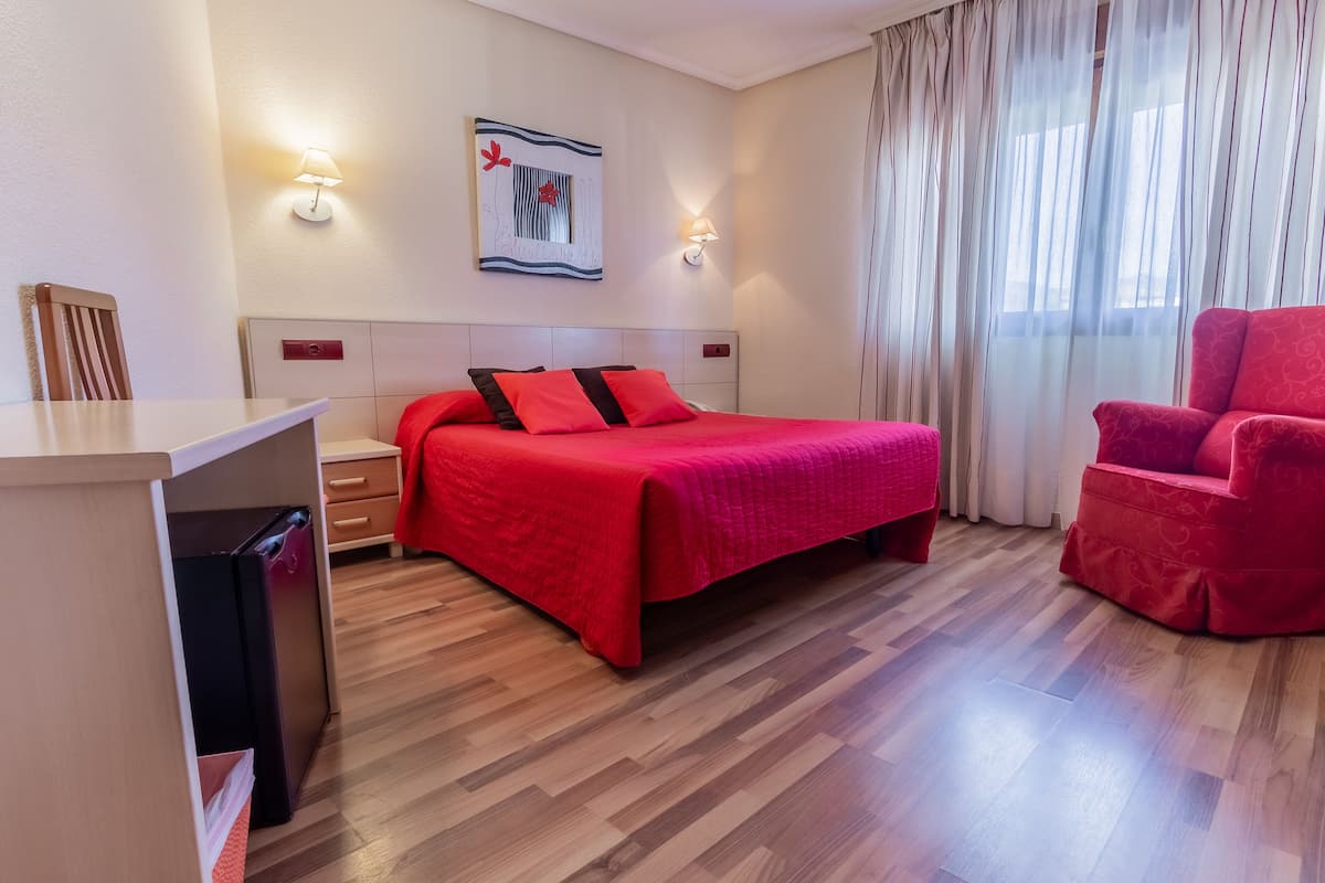 Quarto de hotel com cama, escrivaninha, cadeira e mesa de cabeceira.