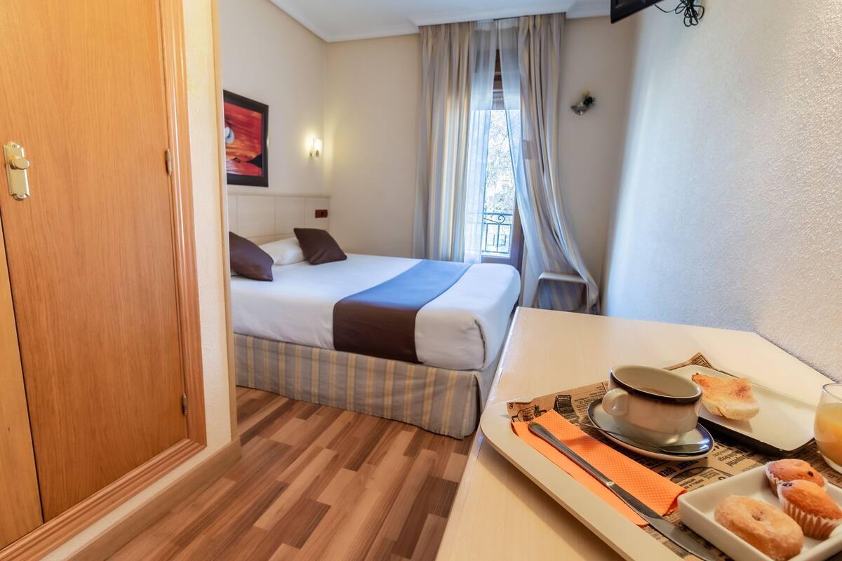 Quarto de hotel com cama, mesa com café da manhã e janela com cortinas.