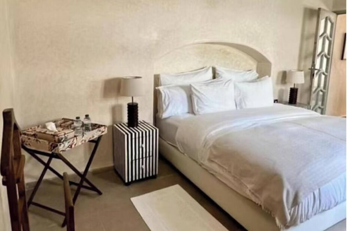 A bedroom with a bed, two bedside tables, a small table with chairs, and a large mirror.