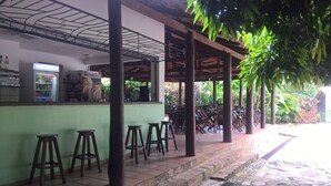 A covered outdoor seating area with wooden stools and a bar counter. - Pousada do Ipê (Goiás)