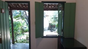 A room with a bed, a small desk, and a window with green shutters. - Pousada do Ipê (Goiás)