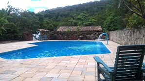 A swimming pool with a stone wall and a tiled roof structure in the background. - Pousada do Ipê (Goiás)