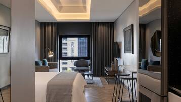 A modern hotel room with a large bed, a desk, a chair, and a mirror. There is a window with a view of a building outside.