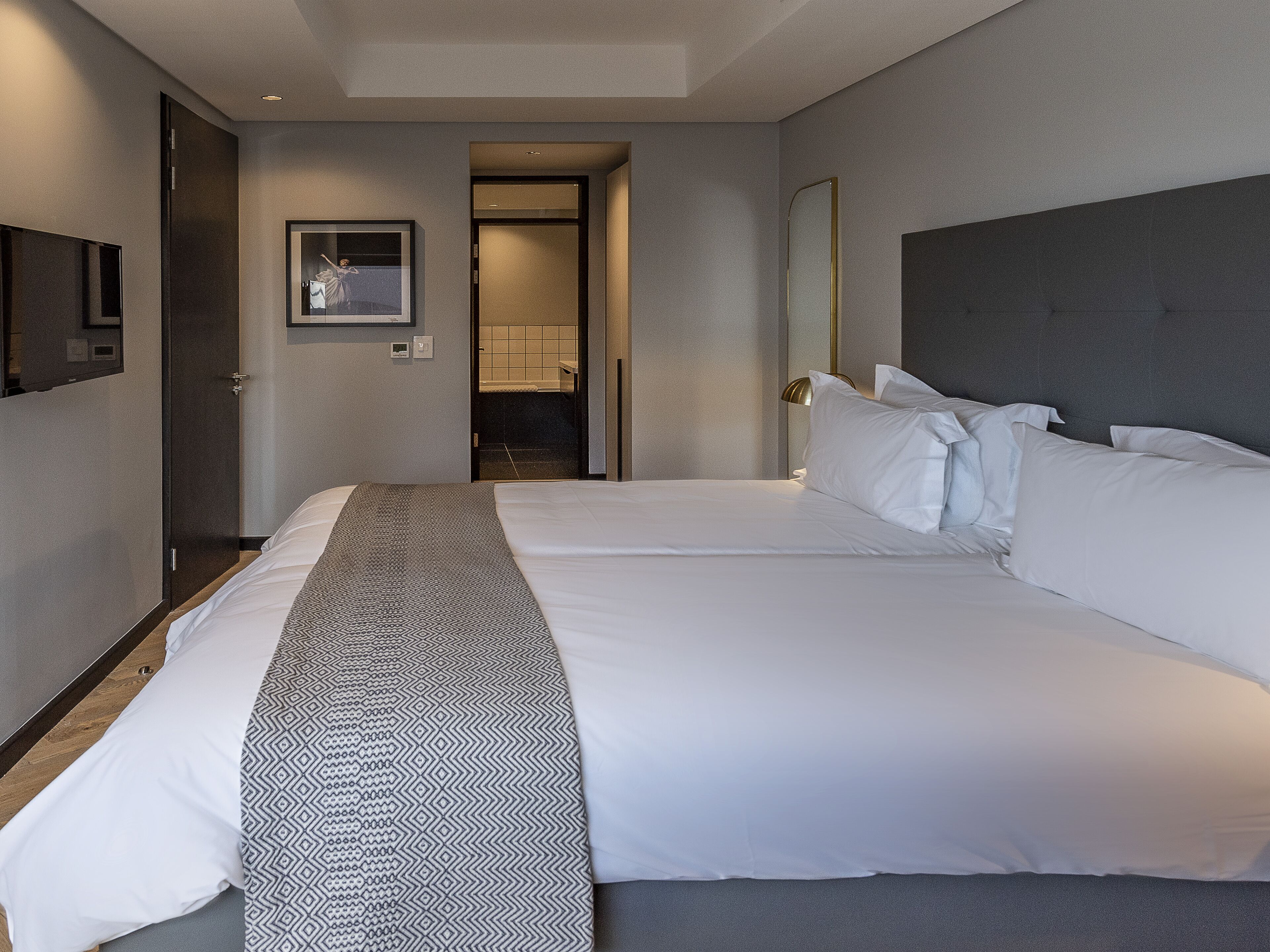 A hotel room with a large bed, a bedside table, a mirror, and a door leading to a bathroom.