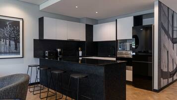 A modern kitchen with a black marble island, bar stools, and stainless steel appliances.