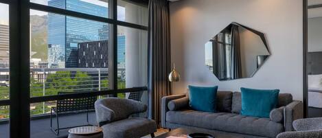 Una sala de estar moderna con un sofá gris, cojines color turquesa, una mesa de centro redonda y un ventanal con vistas a la ciudad.