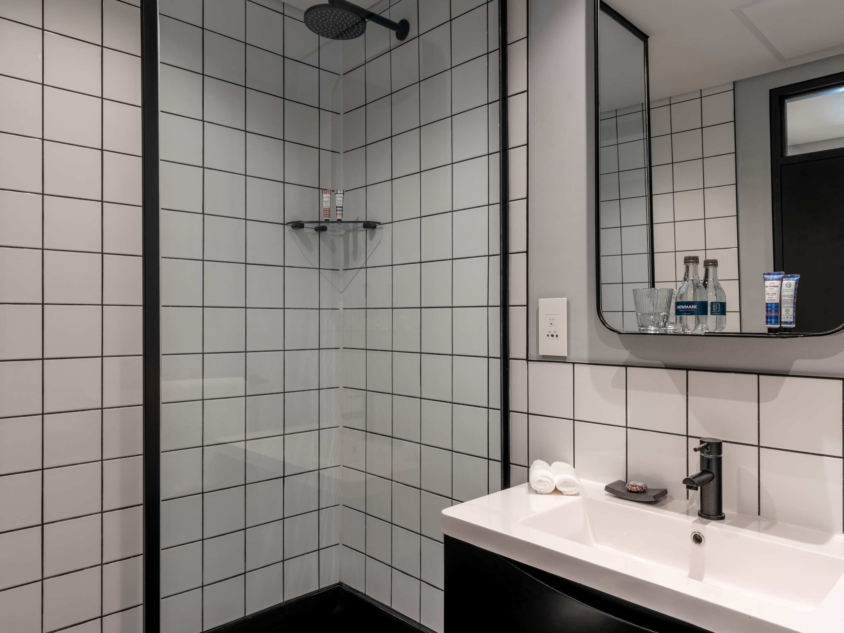 Une salle de bain moderne avec des murs recouverts de carreaux blancs, une baignoire noire, un lavabo blanc et un miroir au-dessus du lavabo.