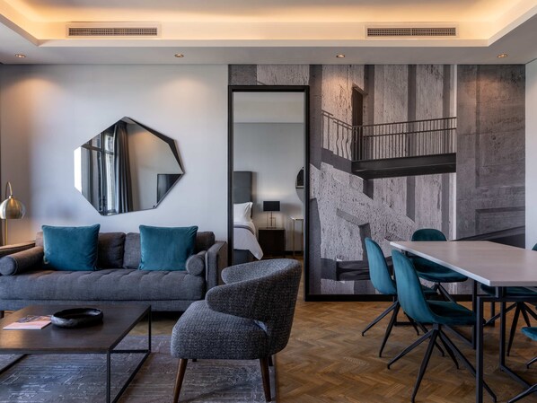 A modern living room with a grey sofa, teal cushions, a coffee table, and a dining area with a white table and teal chairs.