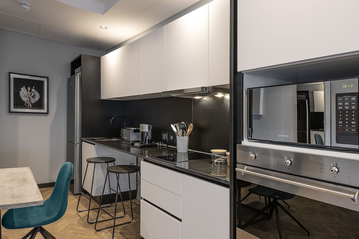Une cuisine moderne avec des armoires blanches, un comptoir noir et un four à micro-ondes en acier inoxydable. Un tableau encadré est accroché au mur et une chaise de couleur turquoise se trouve près de la table à manger.