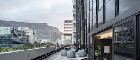 A rooftop terrace with modern seating, a view of the cityscape, and a mountain in the background.