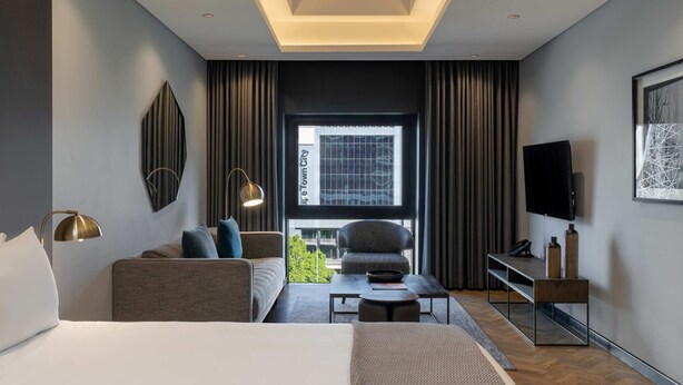 Une chambre d’hôtel moderne équipée d’un lit, d’un canapé, d’une table basse, d’une télévision et offrant une vue sur la ville.