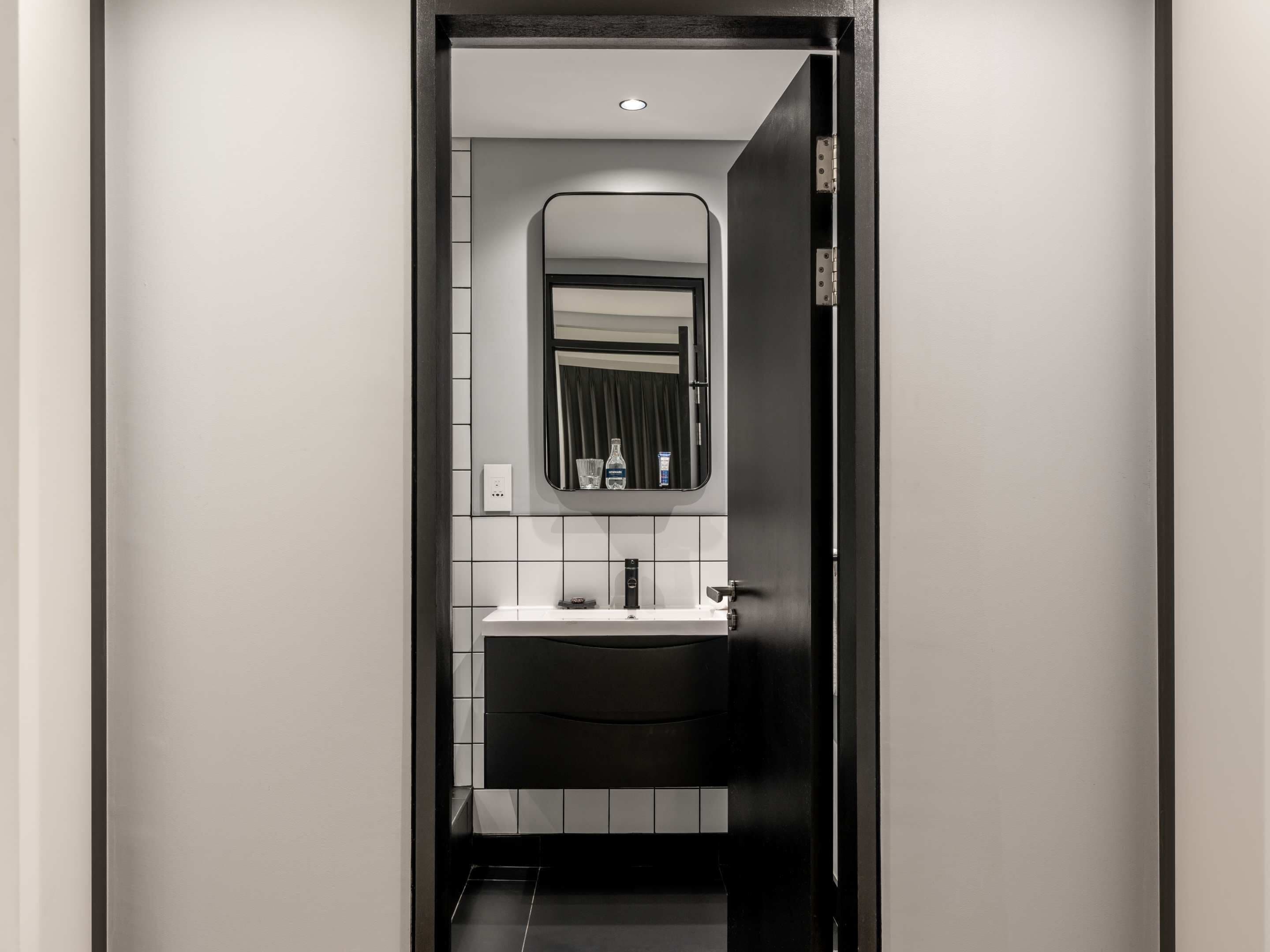 Een moderne badkamer met een zwart wastafelmeubel, witte tegels en een spiegel boven de wastafel.