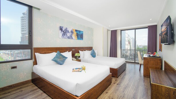 A hotel room with two beds, a wooden desk, a TV, and a large window with a city view. - Grand Sea View Hotel & Spa (Da Nang)