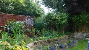 Un jardin agrémenté de diverses fleurs et plantes, un mur de soutènement en pierre et une zone herbeuse.