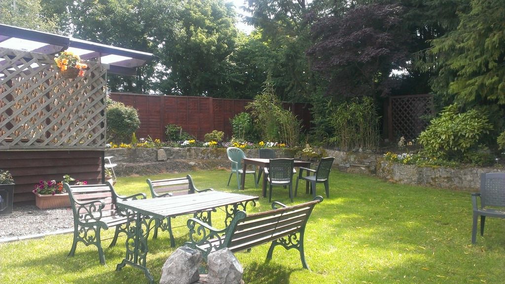 Eine Terrasse mit Tisch und Stühlen, umgeben von einem Garten mit verschiedenen Pflanzen und einem Holzzaun.