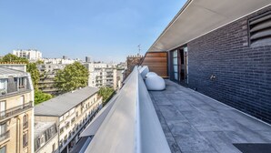 Eine Dachterrasse mit Blick auf umliegende Gebäude, einer Ziegelwand und einem modernen Geländer.