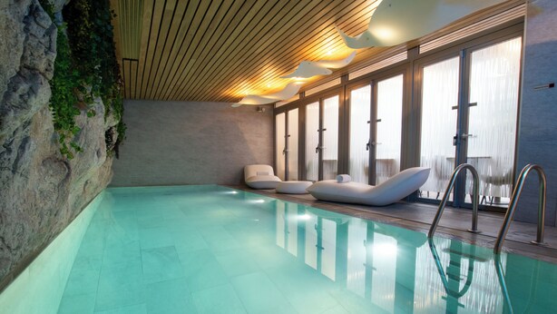 Ein Schwimmbecken mit klarem Wasser, Holzboden und großen Fenstern.