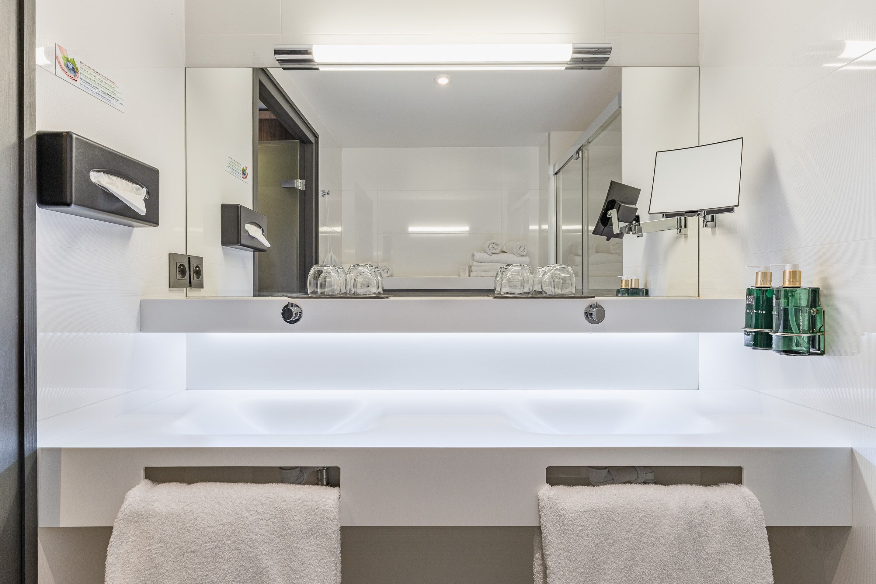 Une salle de bain moderne avec un grand miroir, un lavabo blanc et des porte-serviettes.