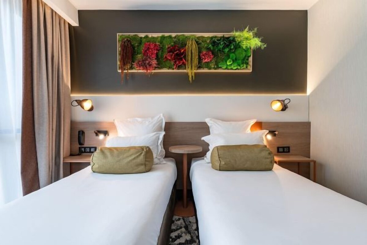 A double room with two beds, a wall-mounted plant, bedside lamps, and a small table.