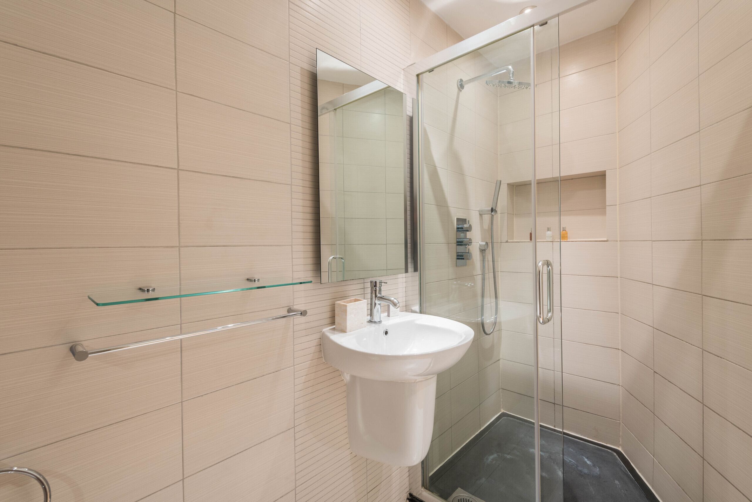 A modern bathroom with a glass shower enclosure, a white sink, and a mirror above it.