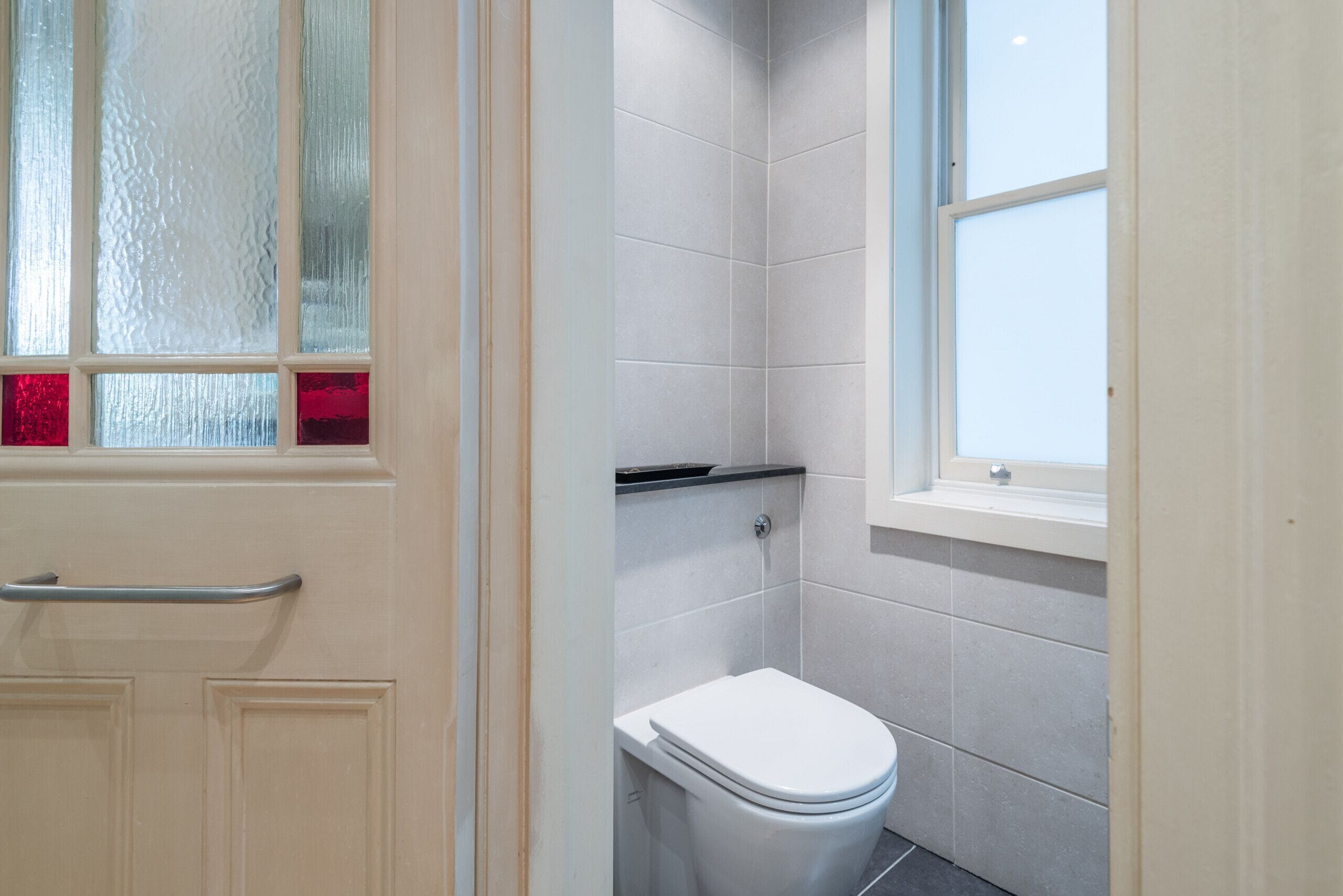 A bathroom with a toilet, a window, and a frosted glass door.