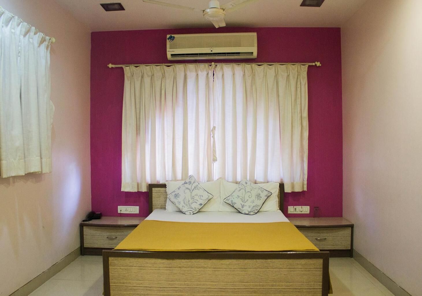 A bedroom with a bed, a bedside table, an air conditioner, and a window with curtains.